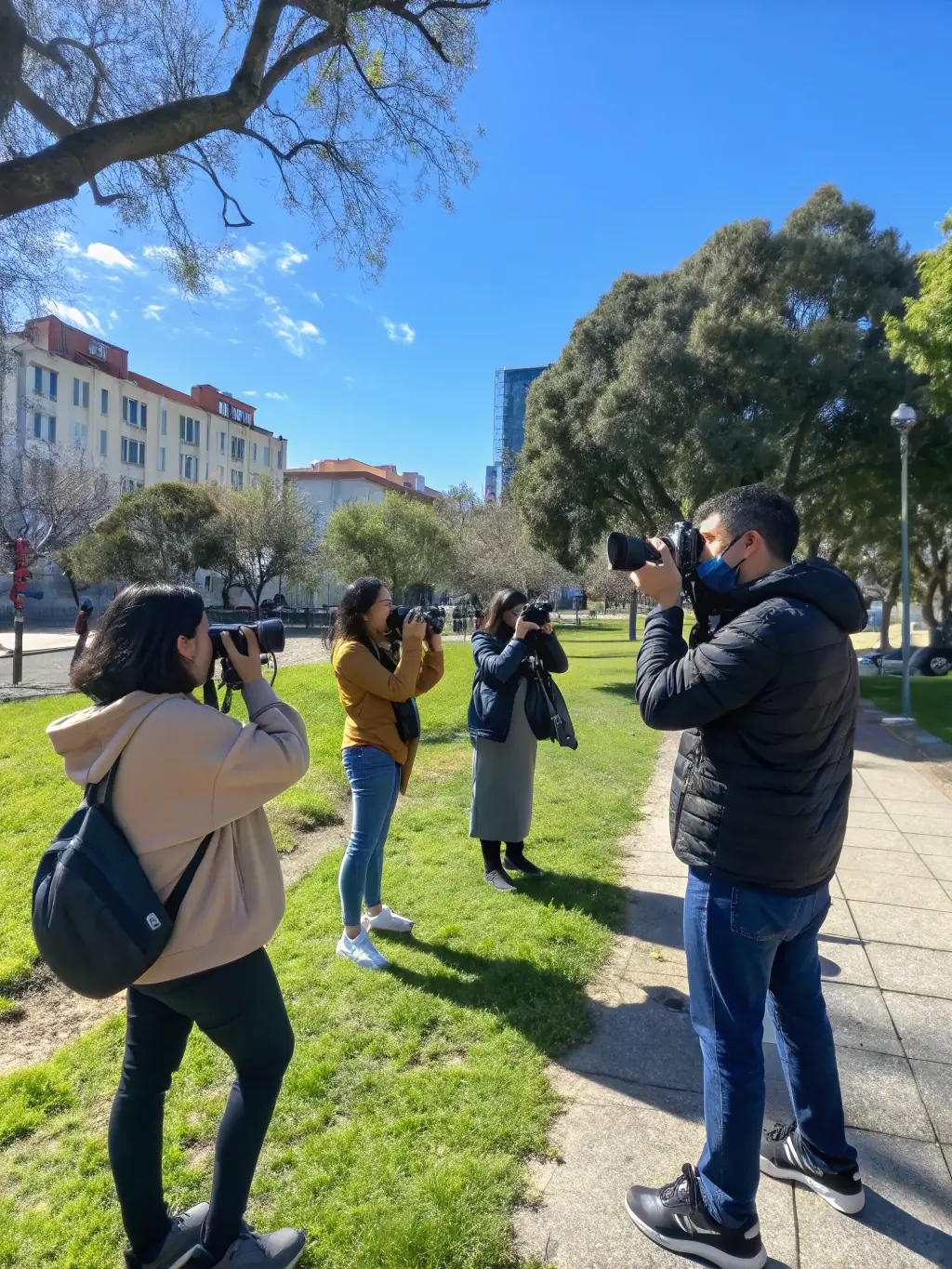 Participants in an ATELIER PLUS photography workshop learning to capture images in a local park, emphasizing the connection between art and nature.